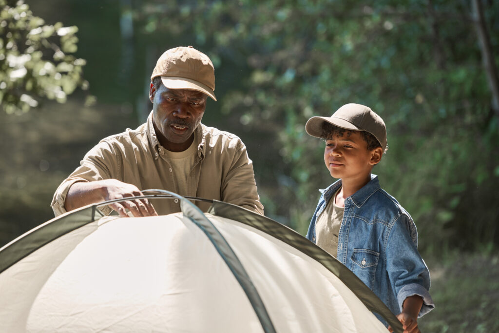 Africian American grandfather and grandson setting up a tent